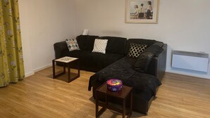 A living room with a black sofa, two patterned throw pillows, a small wooden coffee table, and a framed picture on the wall. - Cozy City Centre 1-bed Apt, 1 Bath, (Coventry)
