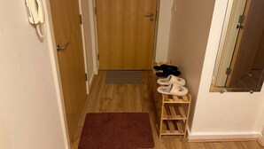 A hallway with a wooden door, a white telephone, a brown rug, and a wooden shoe rack with slippers. - Cozy City Centre 1-bed Apt, 1 Bath, (Coventry)