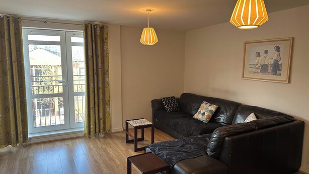 A living room with a black leather sofa, two small tables, and a hanging lamp. - Cozy City Centre 1-bed Apt, 1 Bath, (Coventry)