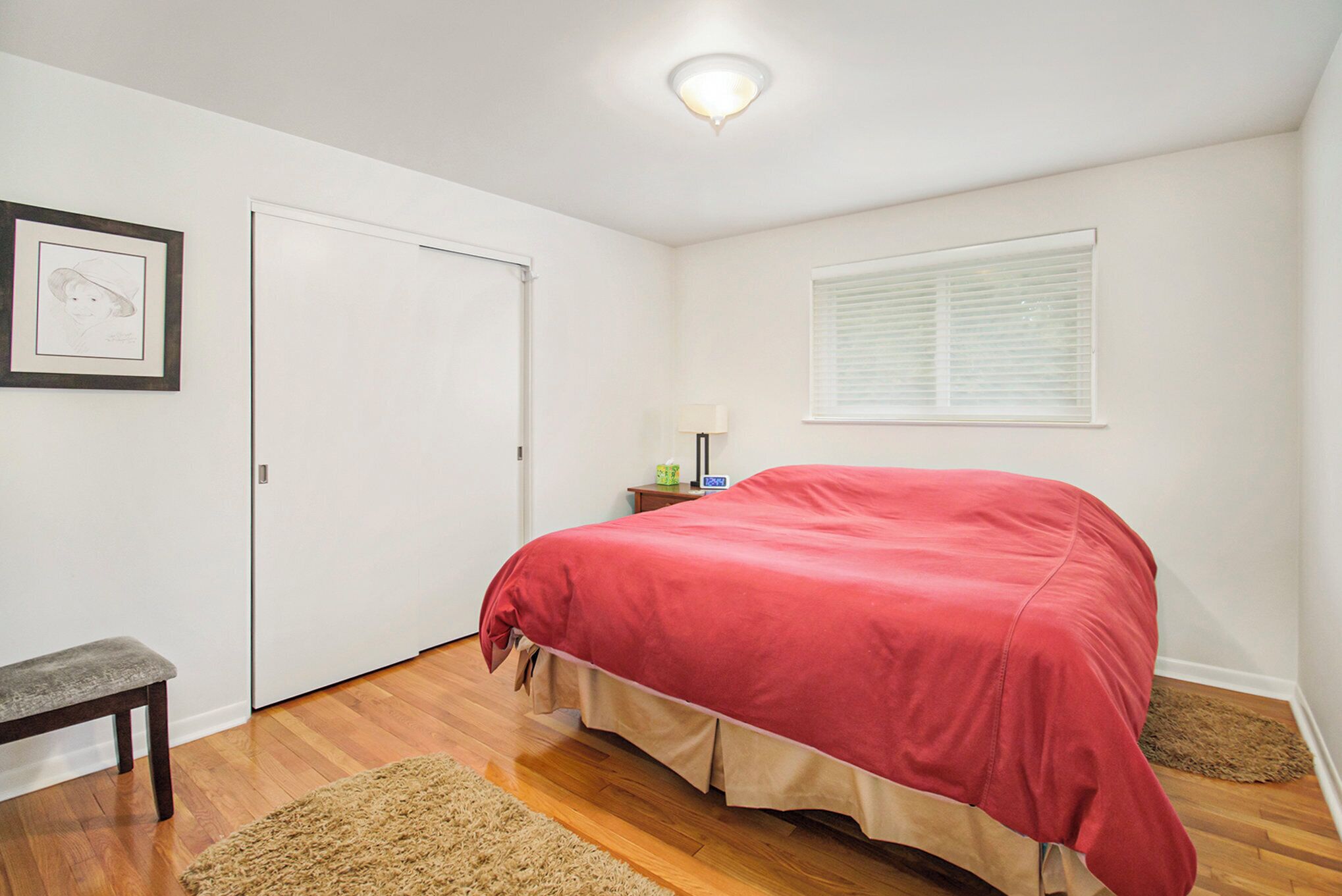Un dormitorio con una cama, un banco, una puerta, una ventana y un cuadro en la pared.