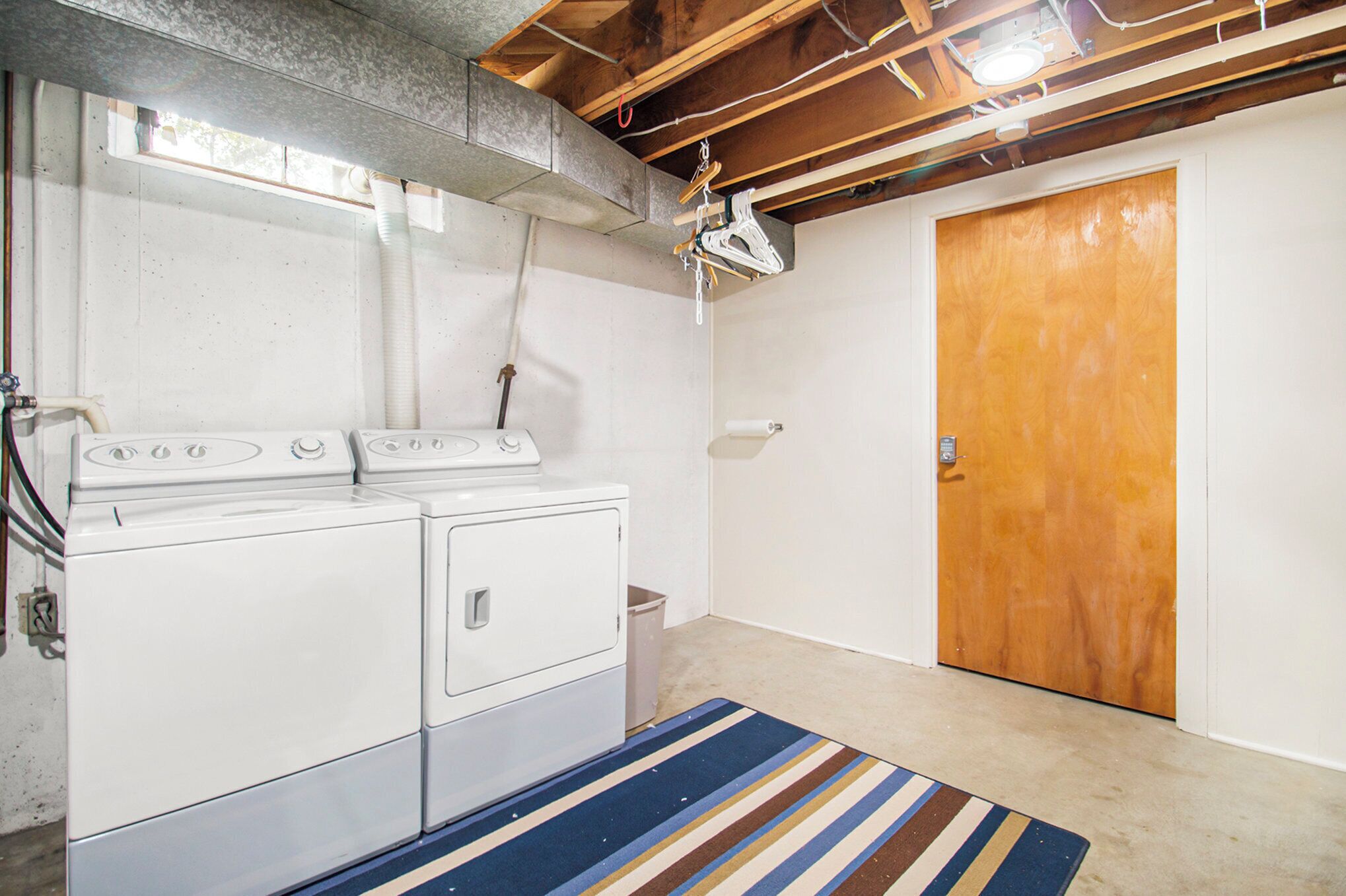 A laundry room with a washing machine and dryer, a wooden door, and a striped rug.