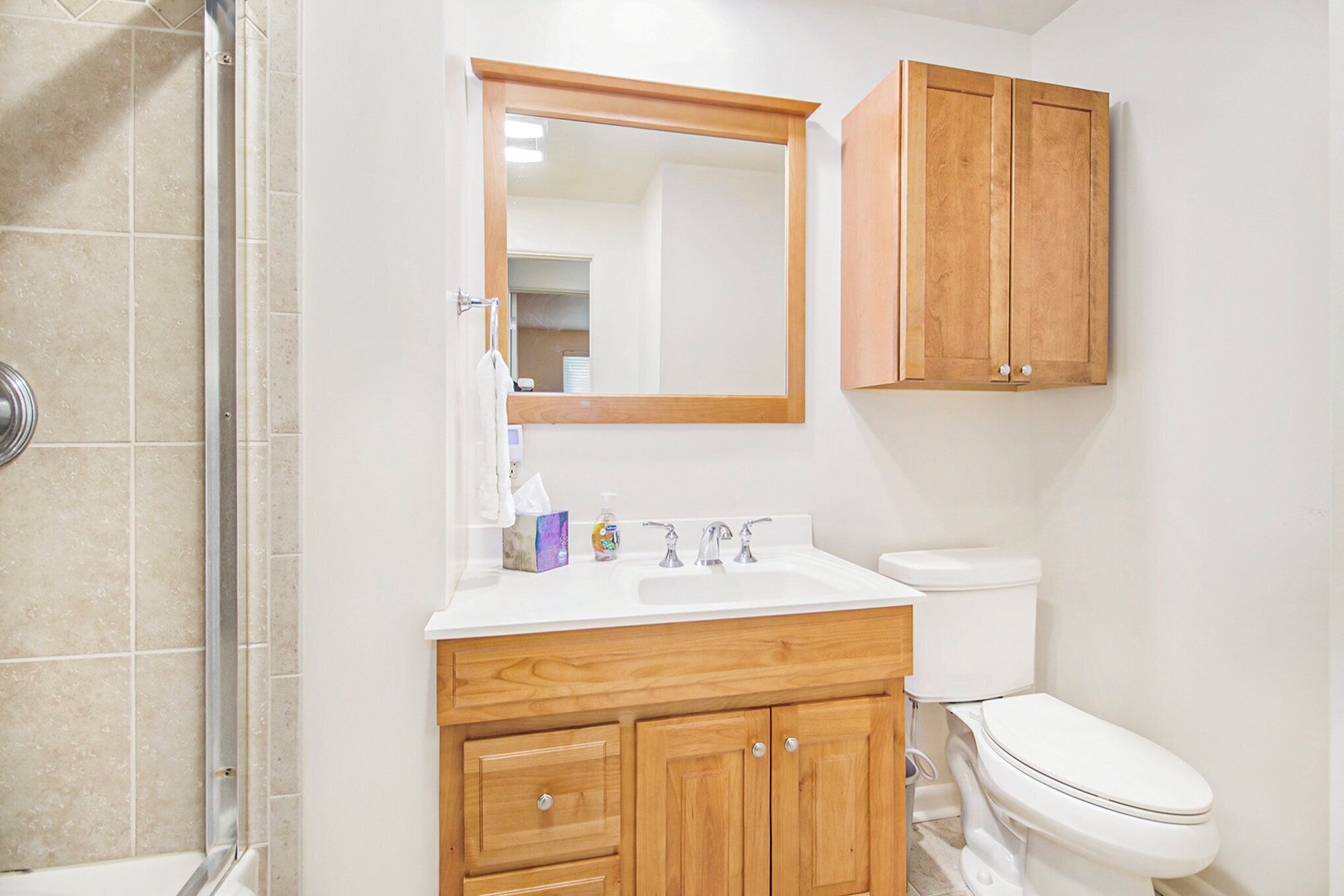 Un baño con ducha, lavabo, espejo y armarios de madera.