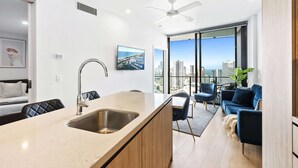 A modern kitchen with a large island, a dining area with a view, and a living space with a sofa and chairs. - Cozy 2 Bedroom Unit in Broadbeach (No Parking) (12801 - 2N - NB) (Broadbeach)