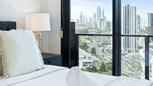 A hotel room with a large window offering a city view, a bed with white linens, and a bedside table with a lamp. - Cozy 2 Bedroom Unit in Broadbeach (No Parking) (12801 - 2N - NB) (Broadbeach)