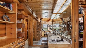 A log cabin interior with a central stone-tiled kitchen area, wooden shelves, and a view of the outdoors. - Quaint 4-bedroom cabin with Loft in Jackson with WiFi access (Jackson)