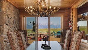 A dining area with a large table, wooden chairs, a chandelier, and a view of mountains through large windows. - Quaint 4-bedroom cabin with Loft in Jackson with WiFi access (Jackson)