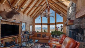 A log cabin interior with a large TV, leather sofas, a fireplace, and a mountain view. - Quaint 4-bedroom cabin with Loft in Jackson with WiFi access (Jackson)