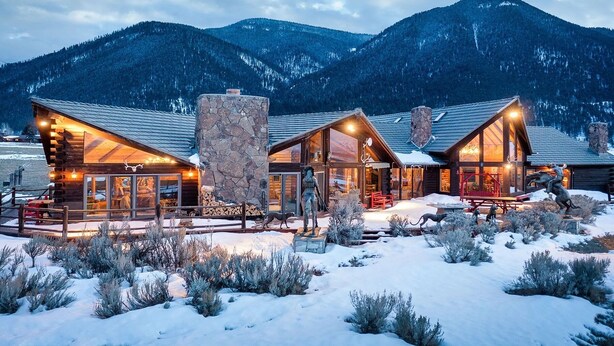 A log cabin with a stone chimney, large windows, and a snow-covered landscape with mountains in the background. - Quaint 4-bedroom cabin with Loft in Jackson with WiFi access (Jackson)