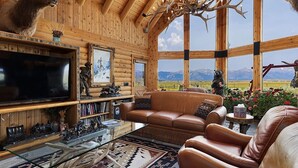 A log cabin interior with a leather sofa, a television, and a large window offering a mountain view. - Quaint 4-bedroom cabin with Loft in Jackson with WiFi access (Jackson)