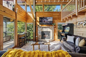A wooden cabin interior with a stone fireplace, a television, and a dining area with a table and chairs. - Best Views in Sevierville! 1b/2ba + Loft! Hot Tub. 15 min to Pigeon Forge! (Sevierville)