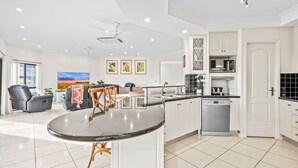 A modern kitchen with white cabinets, a built-in dishwasher, and a dining area with a round table and chairs. - Your Ultimate Escape in Mooroobool- Luxury Tropical Retreat with Pool & Stunning Views – Perfect for Families & Groups! (Mooroobool)