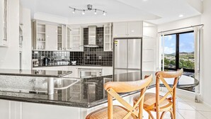 A modern kitchen with white cabinetry, a black countertop, and a large island with two wooden chairs. - Your Ultimate Escape in Mooroobool- Luxury Tropical Retreat with Pool & Stunning Views – Perfect for Families & Groups! (Mooroobool)