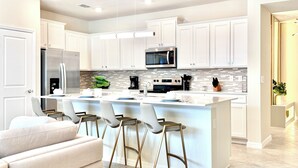 A modern kitchen with white cabinets, a central island with bar stools, stainless steel appliances, and a tiled backsplash. - Spacious 5-bedroom, Star Wars Loft, Pvt Pool, WiFi in brilliant Clermont (Clermont)
