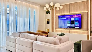 A modern living room with a large flat-screen TV mounted on a wooden wall, a beige sofa, and a chandelier. - Spacious 5-bedroom, Star Wars Loft, Pvt Pool, WiFi in brilliant Clermont (Clermont)