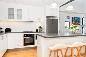 A modern kitchen with white cabinetry, a built-in oven, a stainless steel refrigerator, and a bar area with stools.