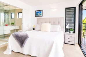 A modern bedroom with a large bed, a glass shower enclosure, and a view of greenery outside.