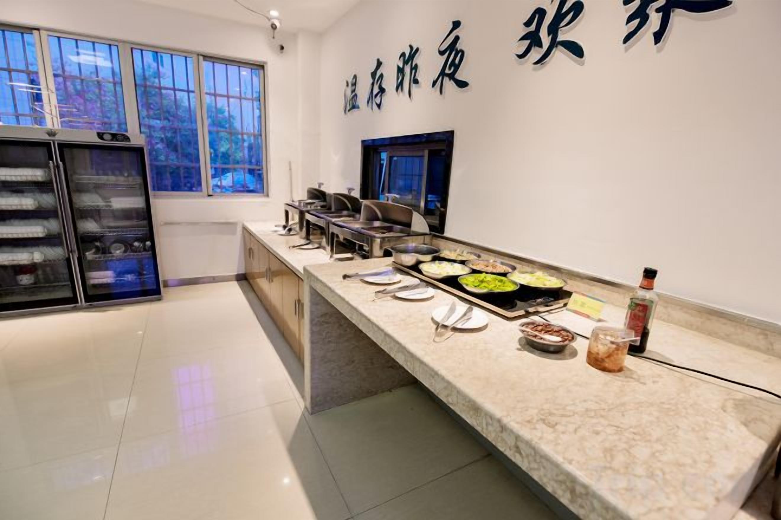 Ein Buffetbereich mit einer Marmorplatte, verschiedenen Speisen, einem Kühlschrank und einer Wand mit chinesischen Schriftzeichen.