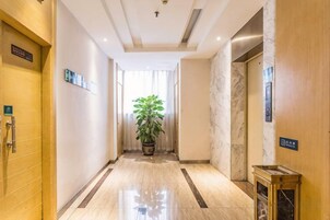 Un pasillo de hotel con suelo de mármol, una planta en maceta y un ascensor.