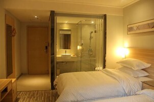 Habitación de hotel con cama, mesita de noche y zona de ducha con paredes de vidrio.
