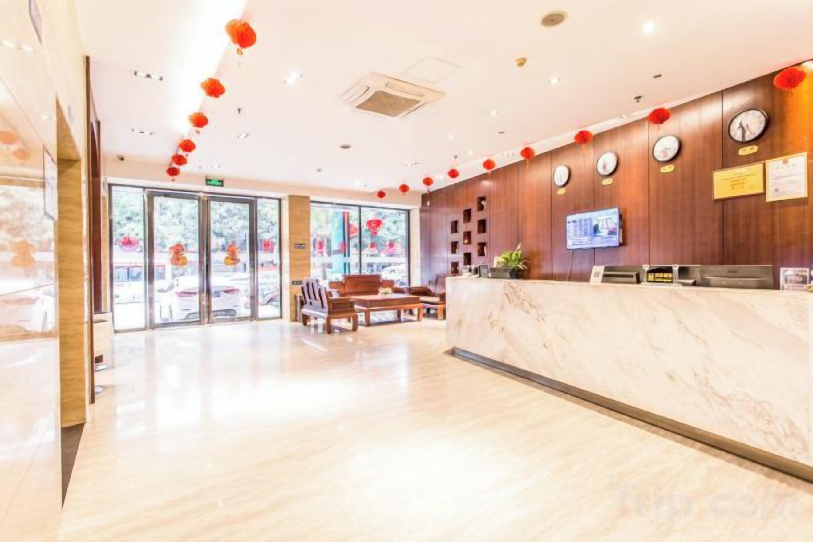 A hotel reception area with a marble counter, wooden paneling, clocks, and a television.