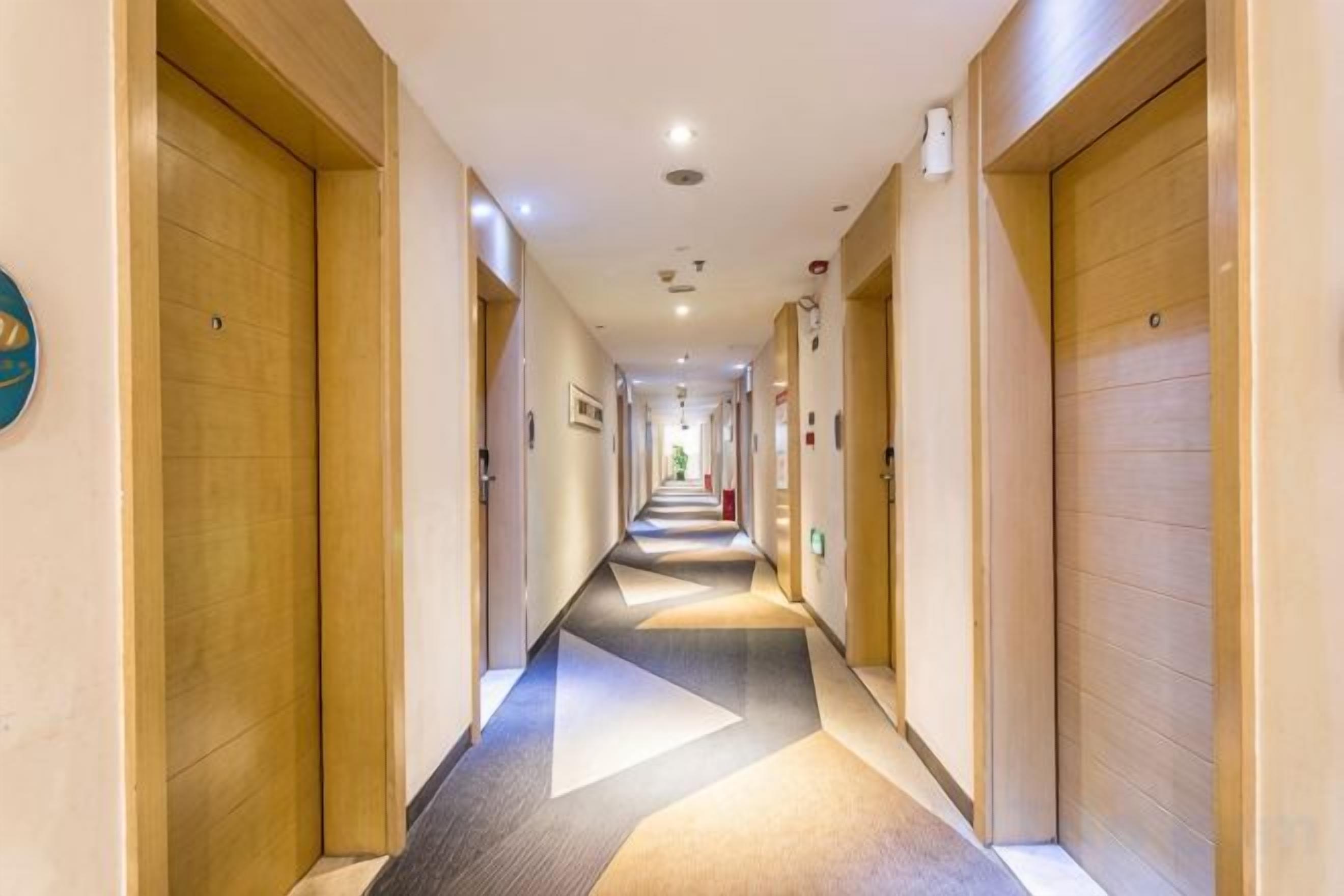 Un corridoio d'hotel con porte in legno, pavimento rivestito di moquette e illuminazione a incasso.