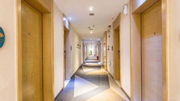 Un corridoio d'hotel con porte in legno, pavimento rivestito di moquette e illuminazione a incasso.