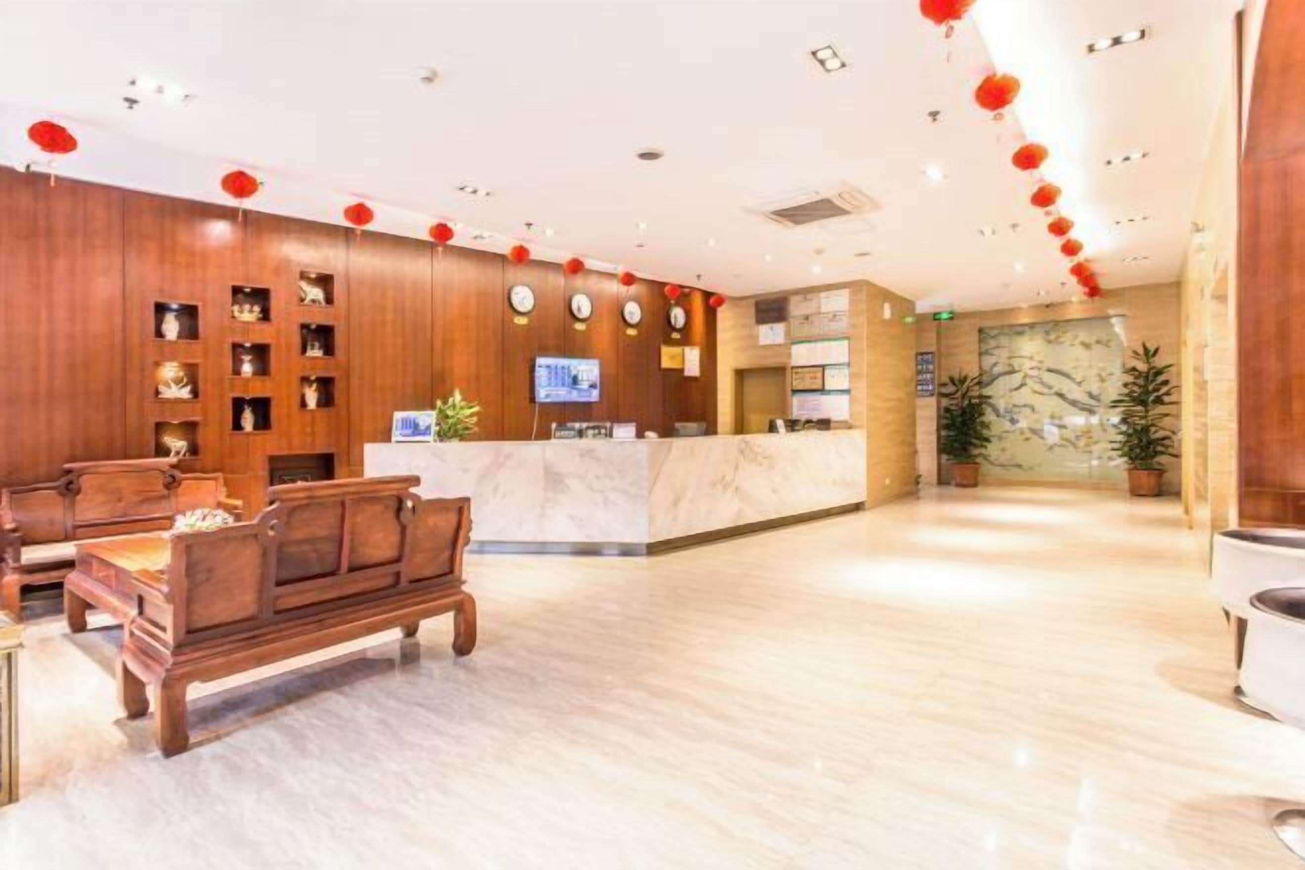 A hotel lobby with wooden paneling, a reception desk, a seating area with a sofa and chairs, and a decorative wall with plants.