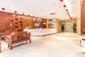 A hotel lobby with wooden paneling, a reception desk, a seating area with a sofa and chairs, and a decorative wall with plants. - Mingdu Hotel (Ningming)