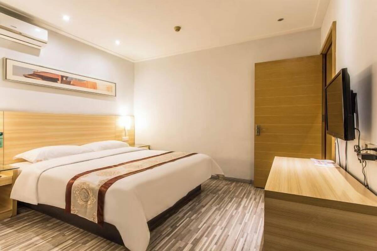 Une chambre d’hôtel avec un lit, une table de chevet, un téléviseur fixé au mur et une porte en bois.