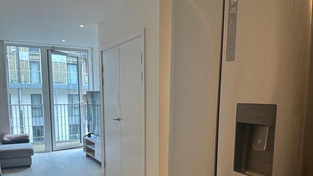 A modern apartment with a large sliding glass door leading to a balcony, a water dispenser, and a minimalist interior. - Cosy Thameside Retreat in North Greenwich (London)