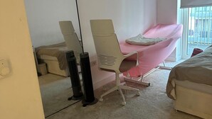 A bedroom with a bed, a bedside table, a chair, and two standing fans. - Cosy Thameside Retreat in North Greenwich (London)