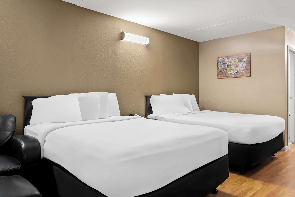 Habitación de hotel con dos camas, un sillón de cuero negro, una lámpara de pared y una obra de arte con un mapa.