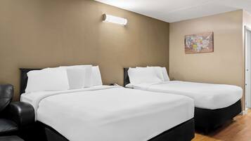 A hotel room with two beds, a black leather chair, a wall-mounted light, and a map artwork.