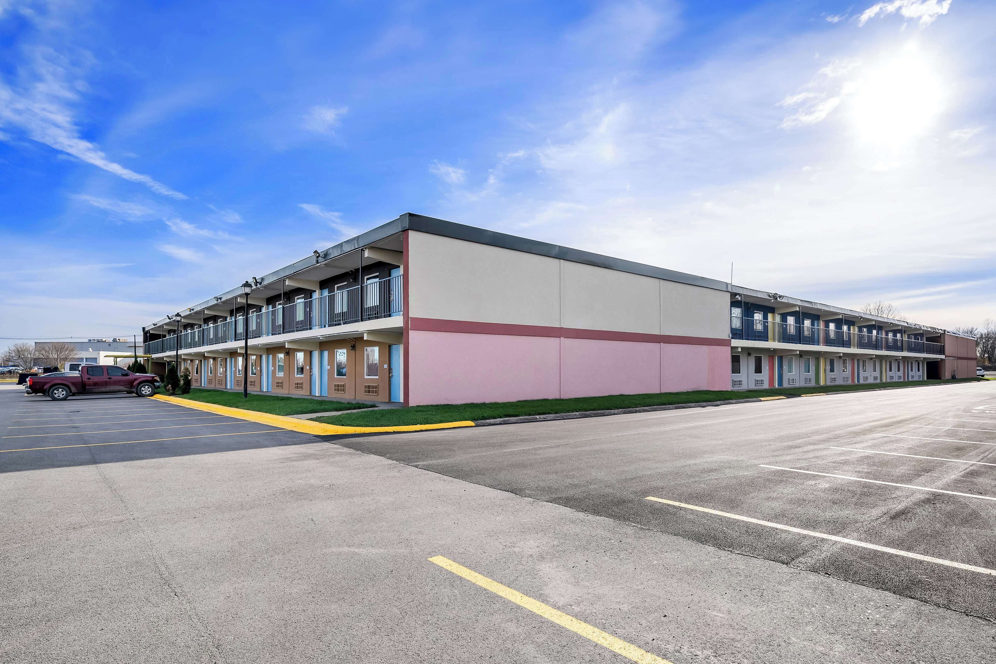 A multi-story motel with a row of rooms on the ground floor and a parking lot in front.