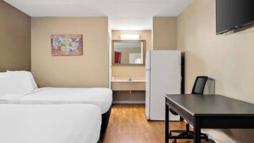 Habitació d'hotel amb dos llits, escriptori, nevera, mirall i televisió penjada a la paret.