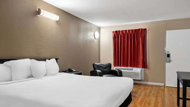 Een hotelkamer met een groot bed, een bureau, een stoel, een rood gordijn en een luchtverkoeler aan de muur.