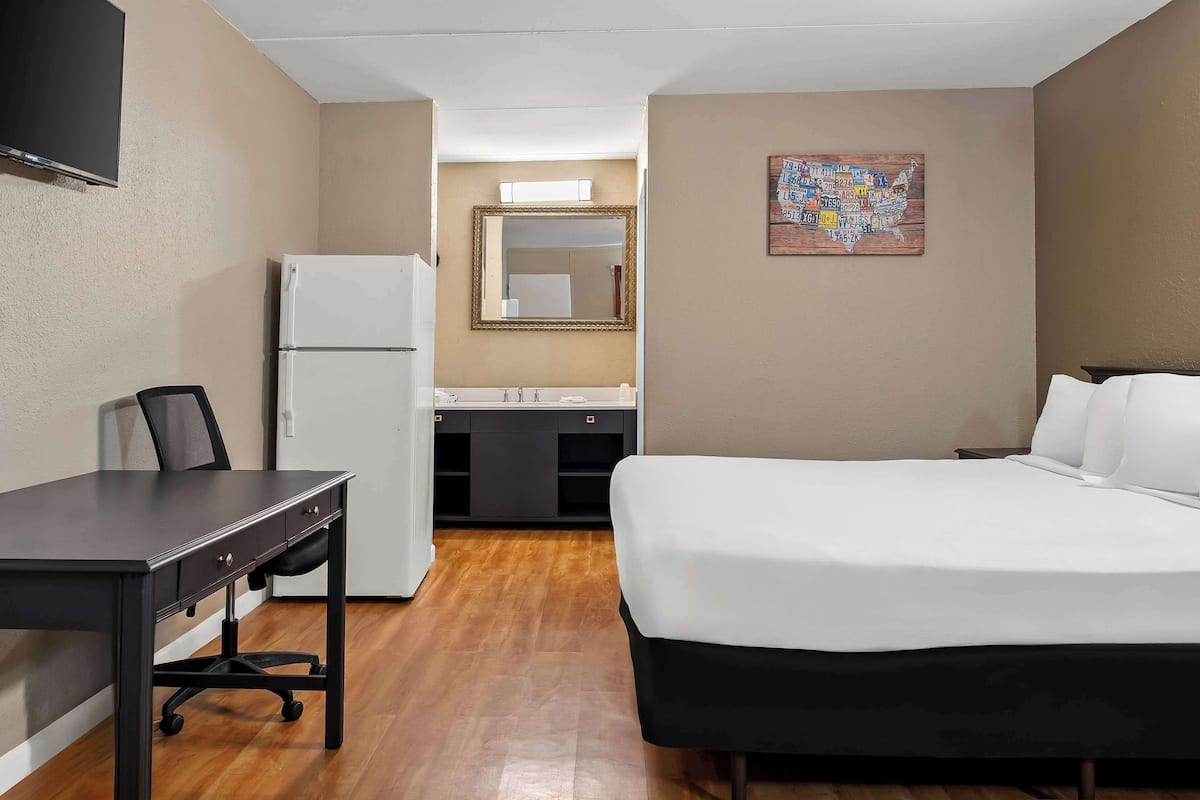 Habitación de hotel con cama, escritorio, silla, refrigerador, espejo y un mapa en la pared.
