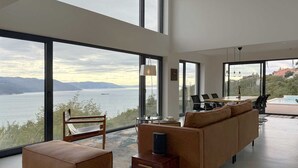 A modern living room with a large window overlooking a body of water and mountains. There is a sofa, a coffee table, and a small side table. - Villa Ena in peaceful location with a sea view (Zagorje)