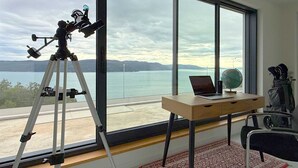 A room with a telescope on a tripod, a laptop, and a globe on a desk by a large window overlooking a body of water. - Villa Ena in peaceful location with a sea view (Zagorje)