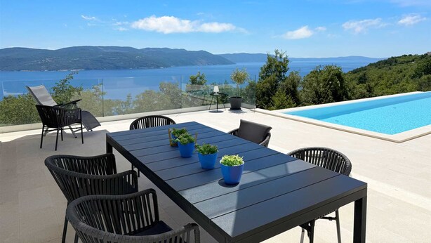 A poolside area with a table and chairs, potted plants, and a view of a lake and mountains. - Villa Ena in peaceful location with a sea view (Zagorje)
