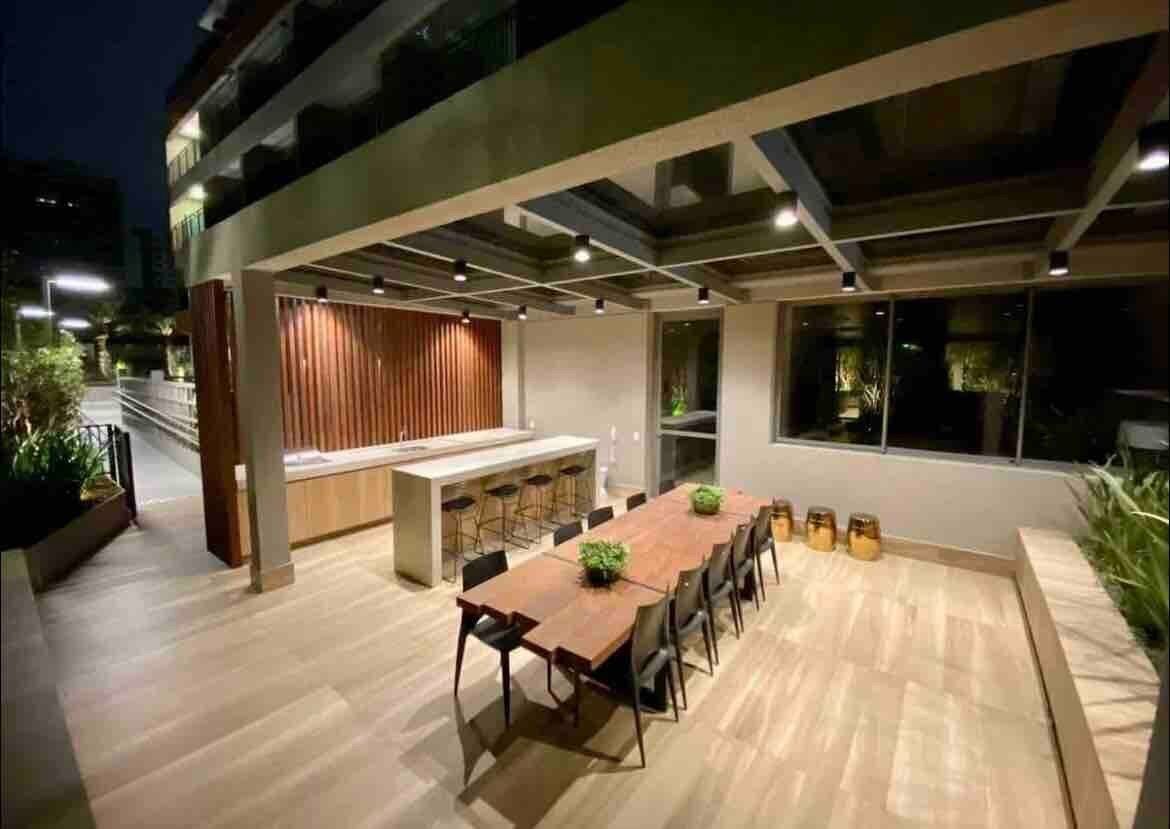 An outdoor dining area with a wooden table and chairs, a bar area, and a modern architectural design with large windows.