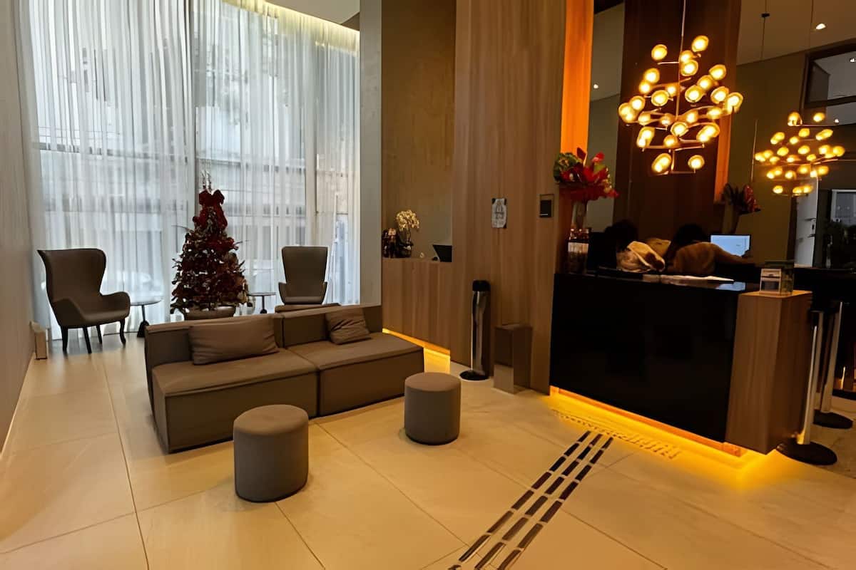 A modern hotel lobby with a reception desk, seating area, and large windows with sheer curtains.