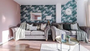 A living room with a sofa, a coffee table, and a wall clock. - Manchester Oasis Retreat - 4 Bedroom House (Manchester)