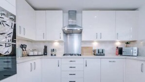 A modern kitchen with white cabinets, a stainless steel range hood, and a black tiled floor. - Manchester Oasis Retreat - 4 Bedroom House (Manchester)