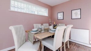 A dining area with a table set for four, white chairs, a wooden table, and a window with a white frame. - Manchester Oasis Retreat - 4 Bedroom House (Manchester)