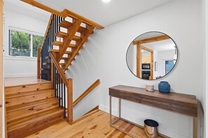 Eine hölzerne Treppe mit modernem Design, ein runder Spiegel an der Wand und ein Holzkonsole mit einer Vase und einer Kerze.