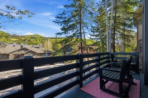 Eine Holzterrasse mit Bank und Tisch, mit Blick auf eine Wohngegend mit Häusern und Bäumen.