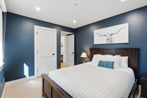 A bedroom with a large bed, a nightstand, a wall-mounted lamp, and a door leading to another room. - Park City & Deer Valley, 3 BR/3BA, Walk to Park City, 2 car garage. (Park City)