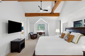 A bedroom with a large bed, a desk, a chair, a television, and a ceiling fan.