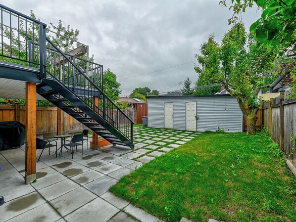A backyard with a patio, a covered seating area, a small shed, and a wooden fence. - Bright 2-Bed Ground Suite | Steps to PNE & Transit (Vancouver)